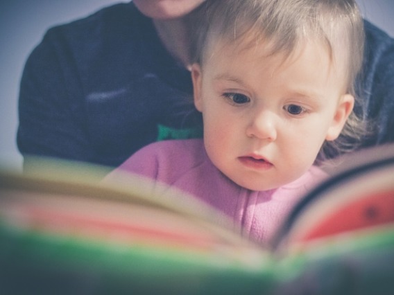 Infant in adult's lap in front of open book for story time