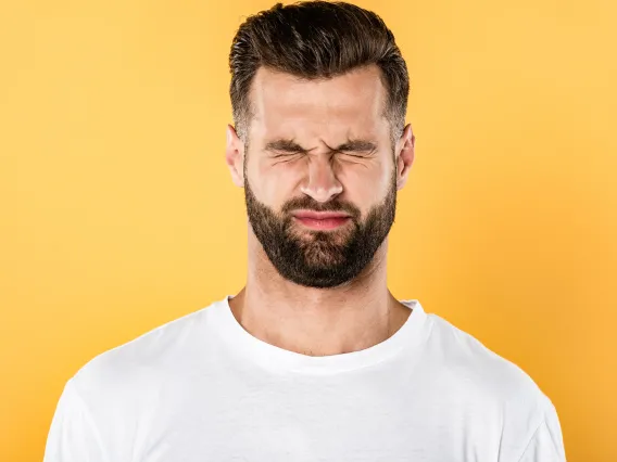 Squinting brunette caucasian male in white T-shirt in front of yellow background 