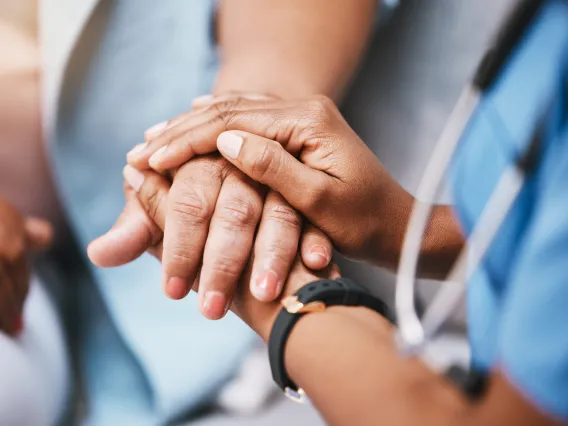 Close-up of doctor in blue scrubs with stethoscope holding a patient's hand