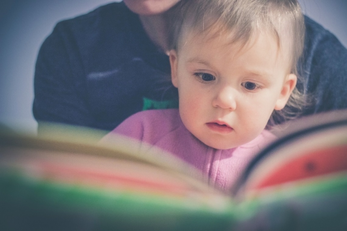 Infant in adult's lap in front of open book for story time