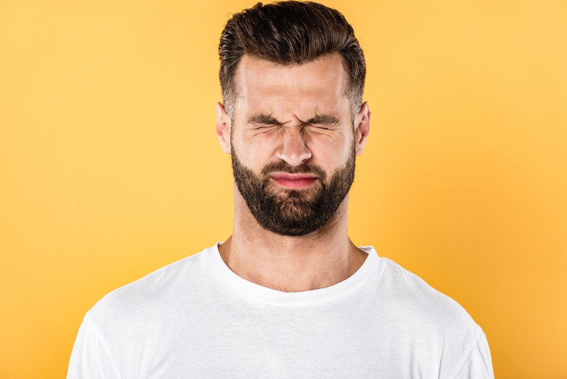 Squinting brunette caucasian male in white T-shirt in front of yellow background 