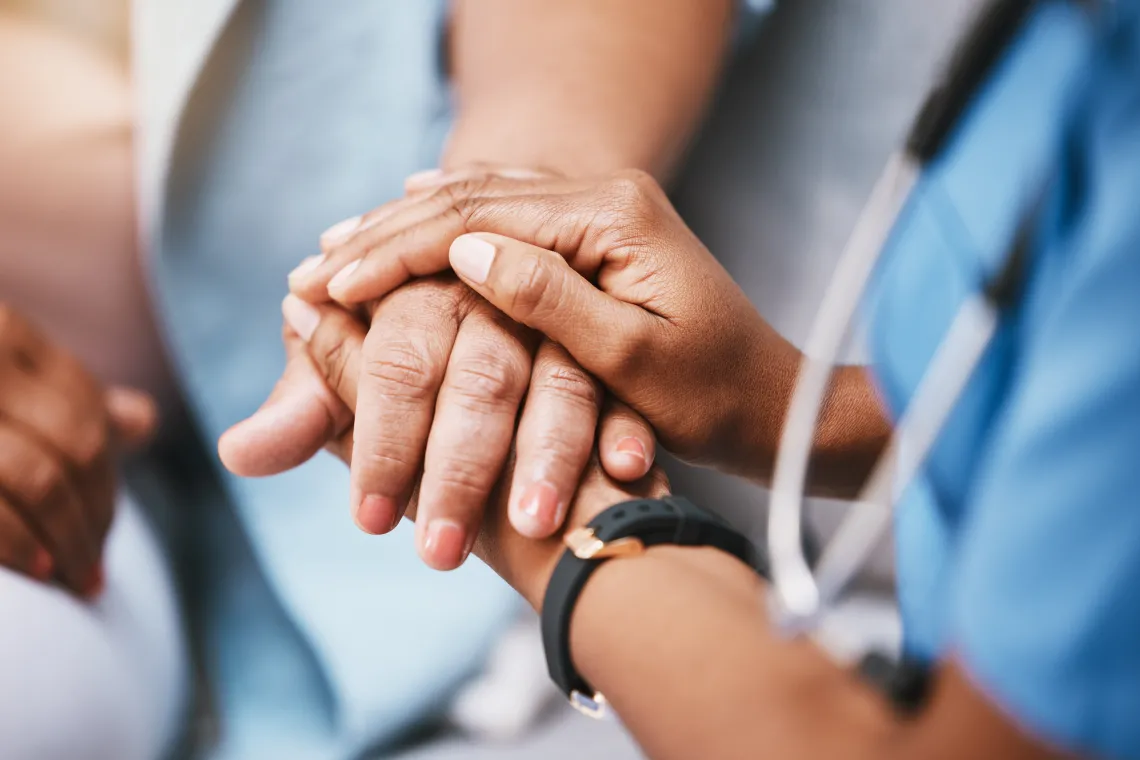 Close-up of doctor in blue scrubs with stethoscope holding a patient's hand