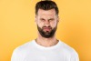 Squinting brunette caucasian male in white T-shirt in front of yellow background 
